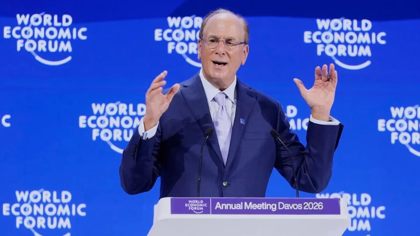 Un hombre con traje azul gesticula mientras habla ante un atril con el rótulo World Economic Forum, Annual Meeting Davos 2026.
