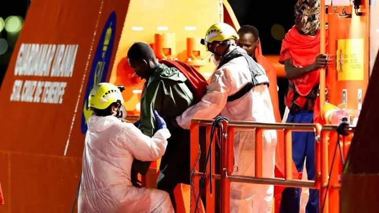 Equipos de rescate con trajes de proteccion ayudan a un migrante a desembarcar de una lancha de salvamento por la noche