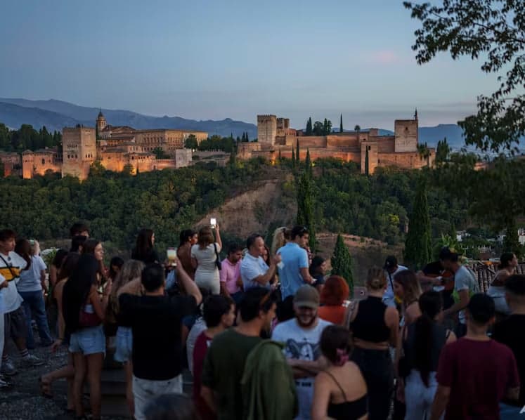 Tourists gather at a Granada viewpoint at dusk to watch the illuminated Alhambra palace and fortress complex
