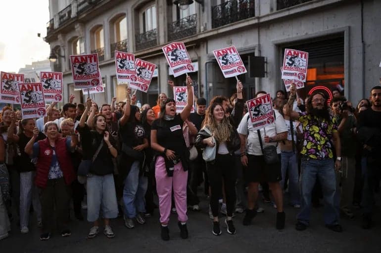 A group of protesters raise signs during a street demonstration in Spain at dusk
