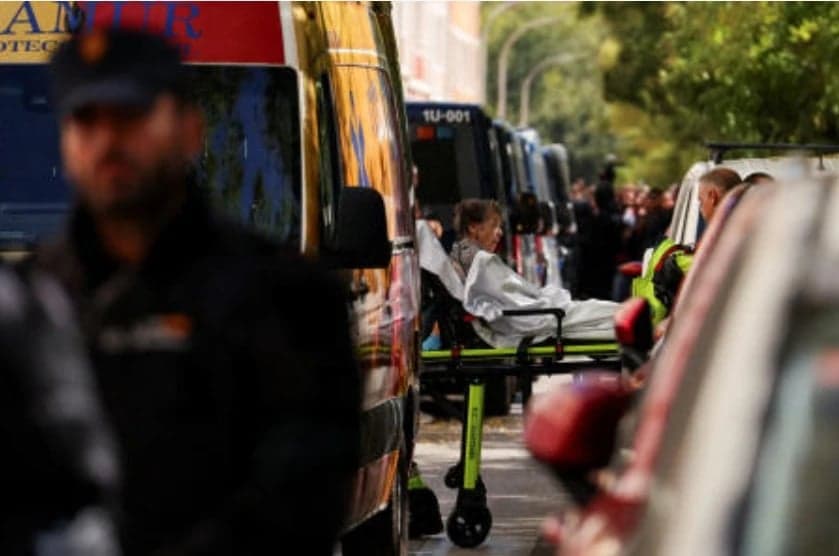 Una mujer mayor es trasladada en camilla junto a vehiculos de emergencia mientras un policia vigila en primer plano