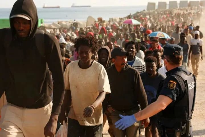 A group of migrants walks alongside a National Police officer on a beach in Ceuta
