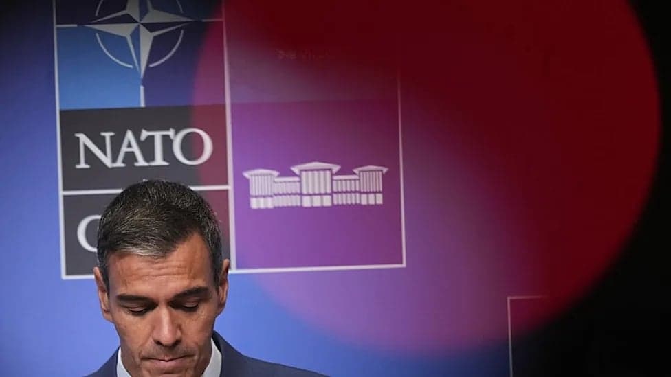 Pedro Sanchez con la mirada baja ante un fondo con los logotipos de la OTAN