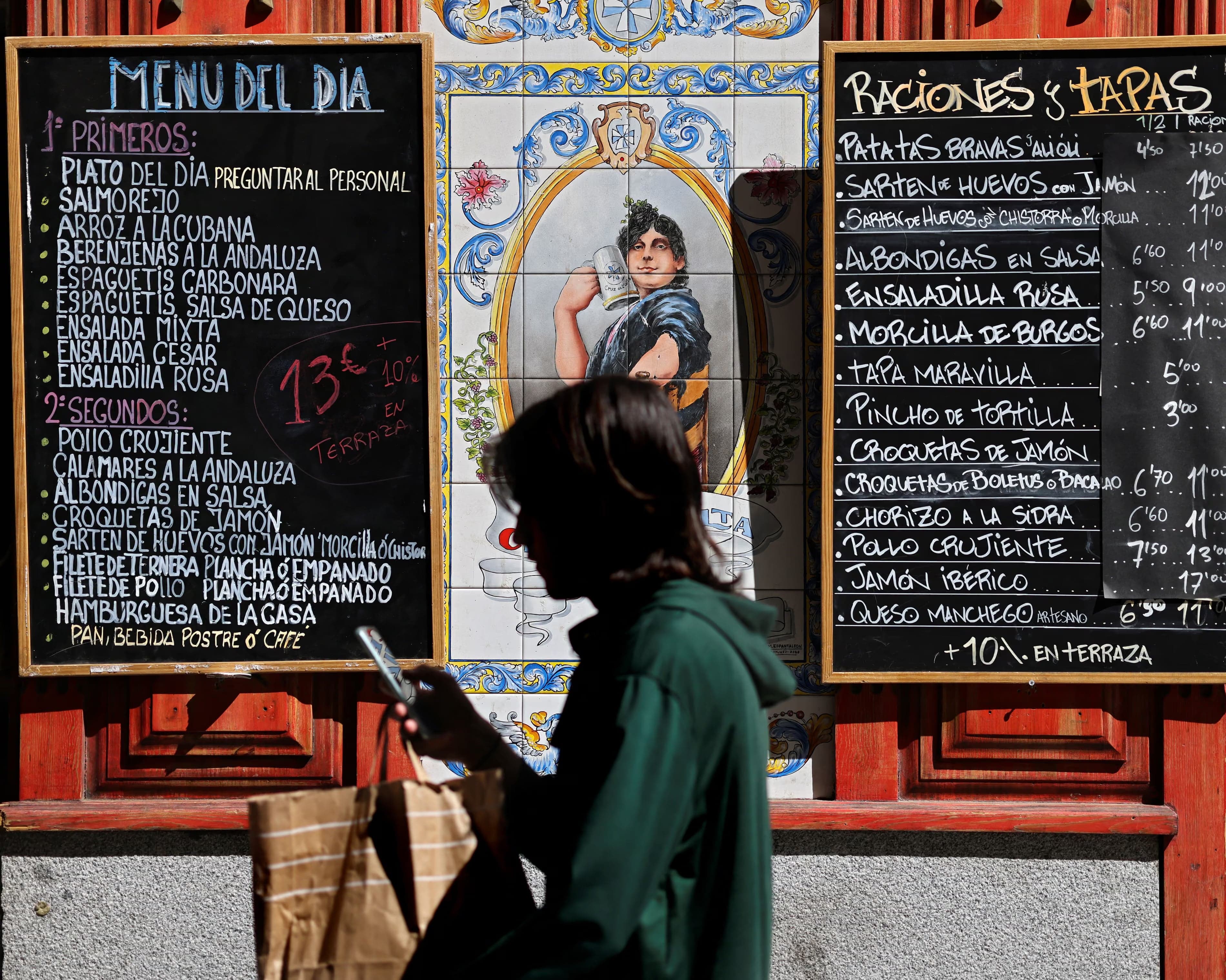 A woman walks past a chalkboard advertising a restaurant's menu del dia in Spain