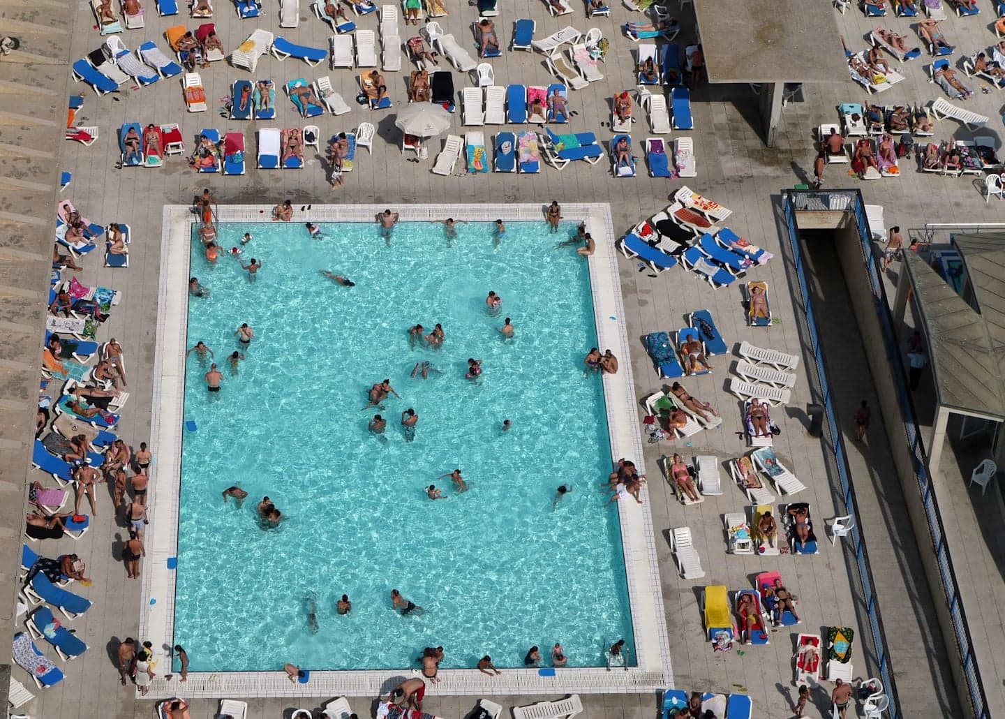 Aerial view of a crowded municipal swimming pool in Spain surrounded by sunbathers on loungers