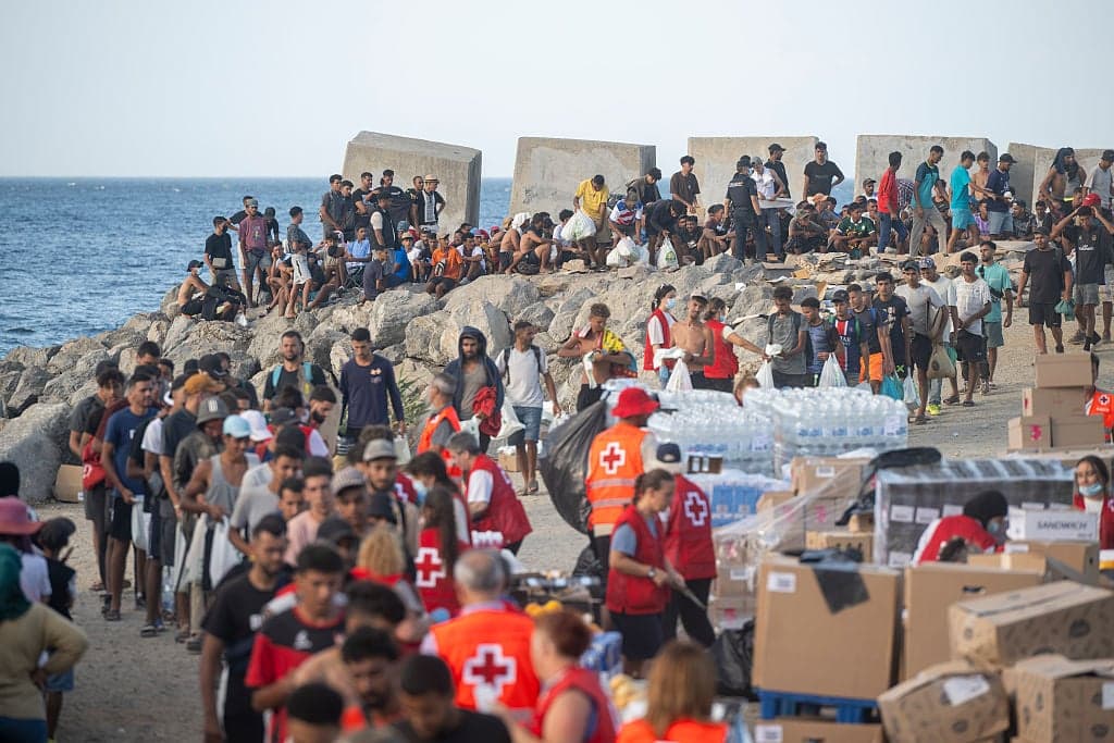 Voluntarios de Cruz Roja reparten agua y suministros a un grupo de migrantes junto al rompeolas de Ceuta