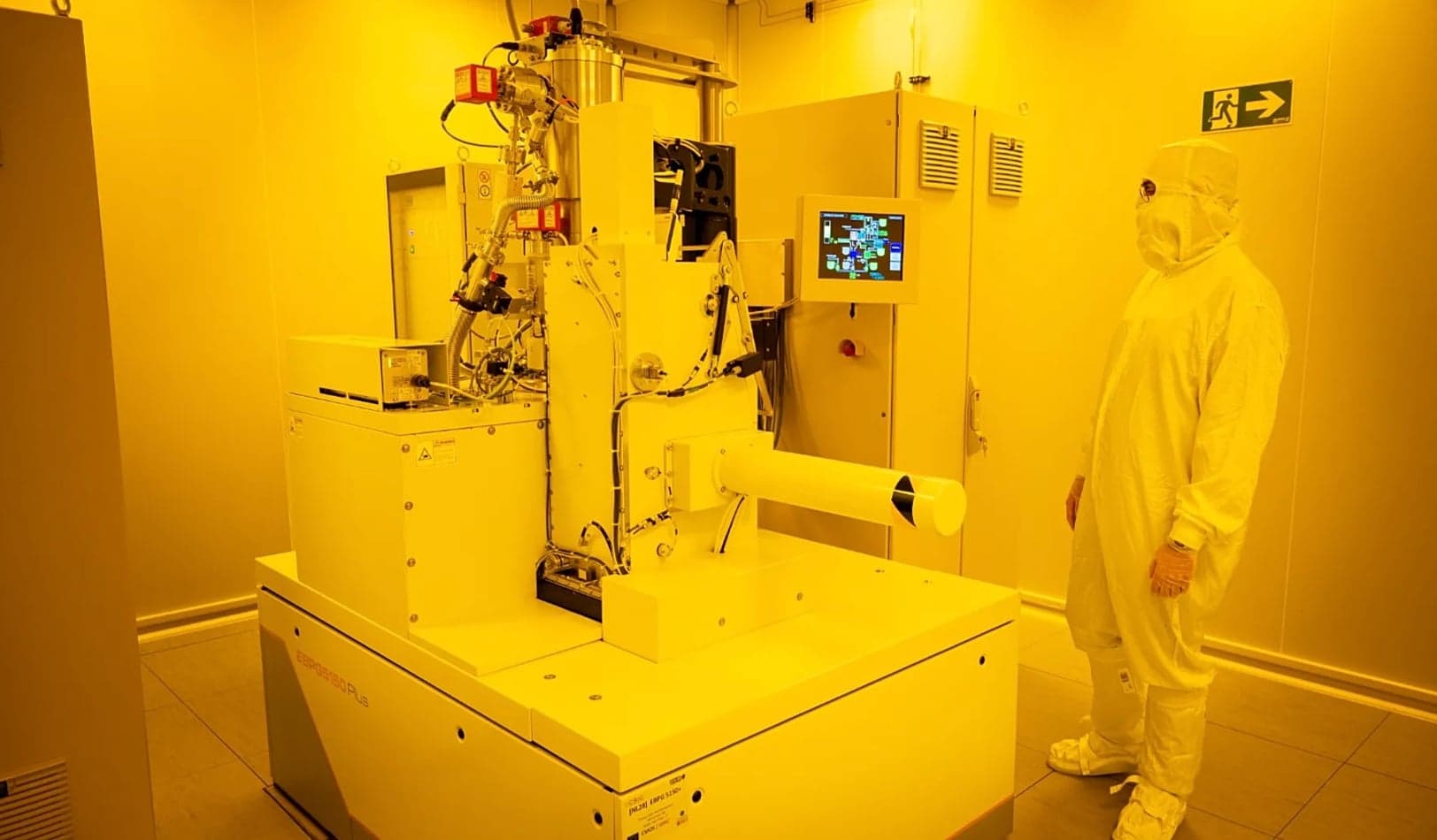 Un tecnico con traje de sala blanca observa un equipo de litografia por haz de electrones en un laboratorio de nanofabricacion