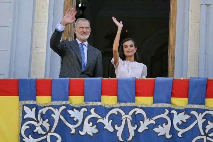 King Felipe VI and Queen Letizia wave from a balcony decorated in Spain's colors