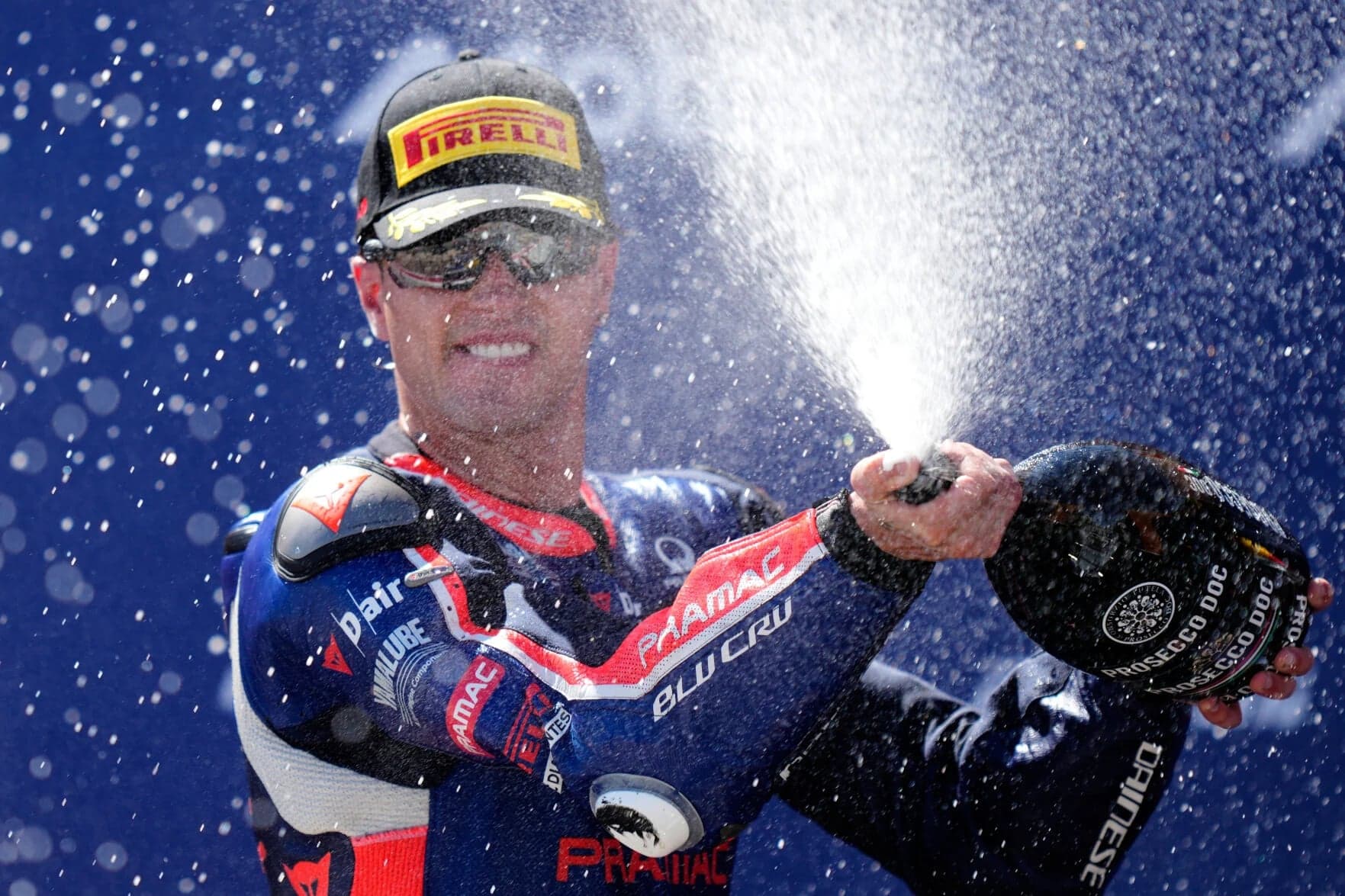 El piloto Izan Guevara celebra en el podio rociando cava, con gorra de Pirelli y mono del equipo Pramac