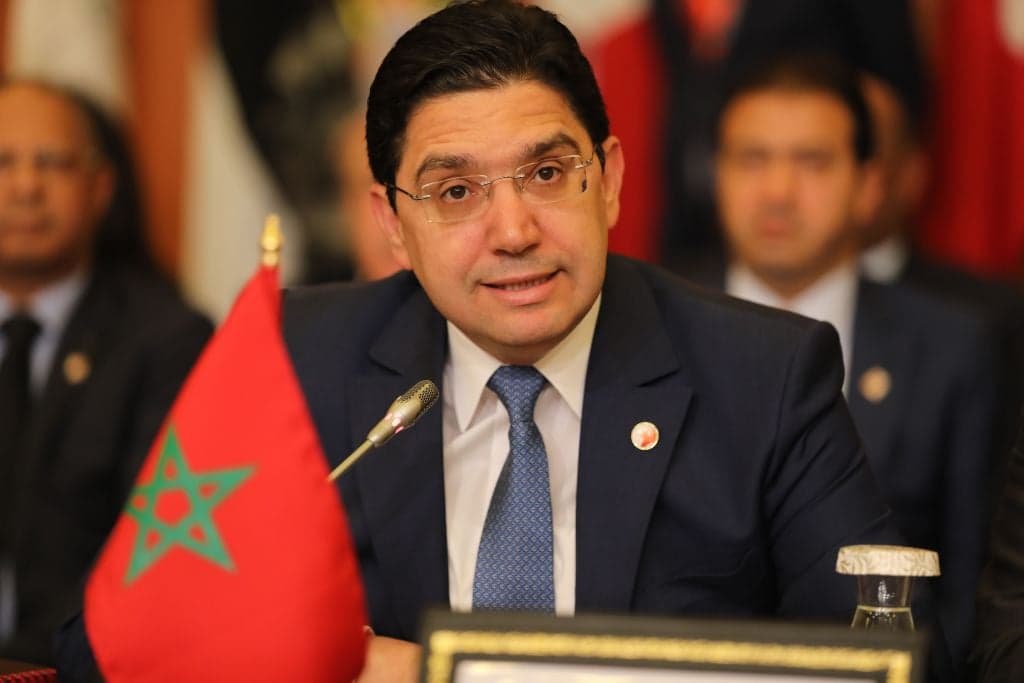 Moroccan Foreign Minister Nasser Bourita speaks in front of a Moroccan flag at an international meeting