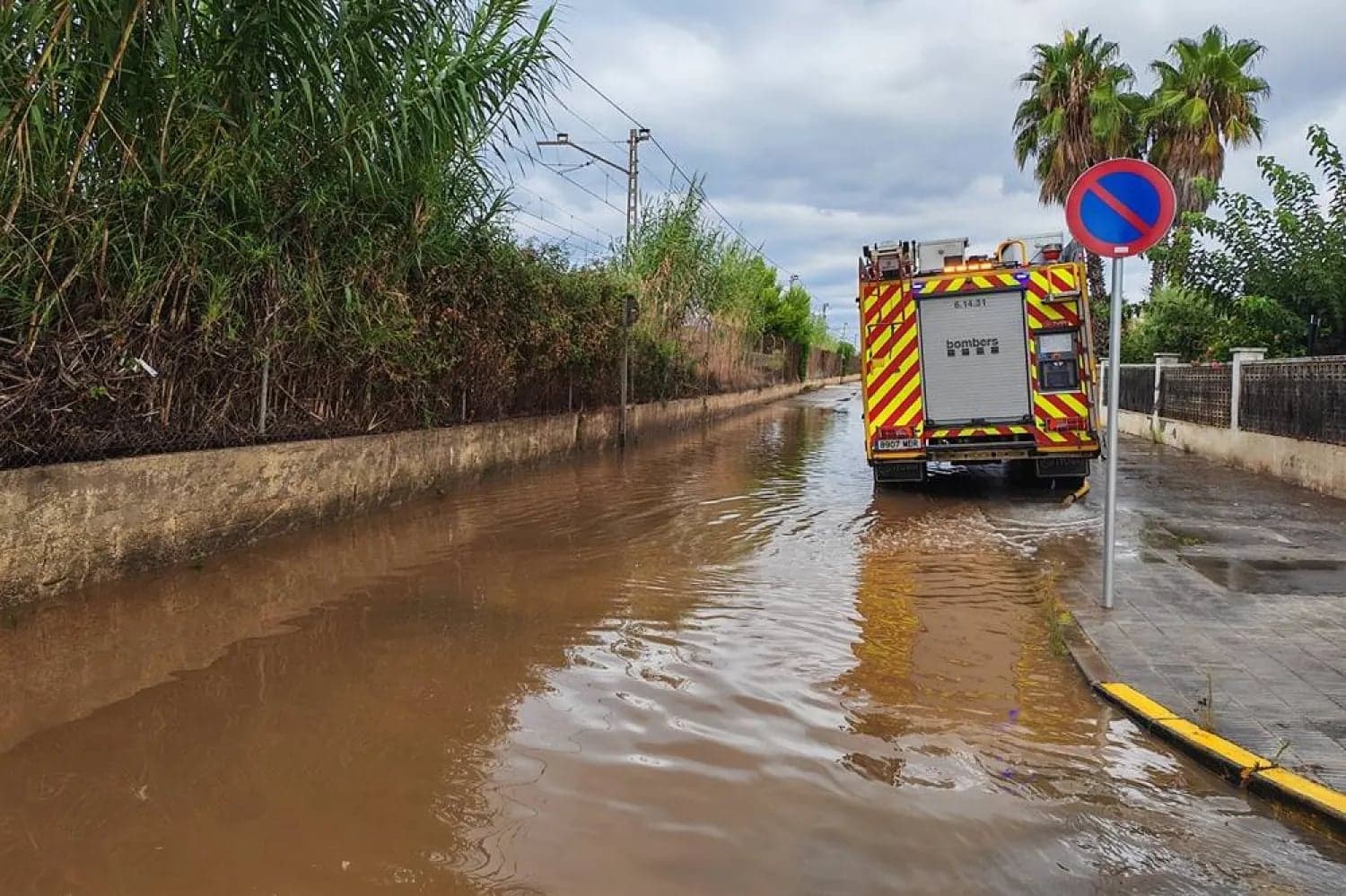 Un camion de bomberos circula por una calle inundada junto a palmeras tras las lluvias torrenciales en Tarragona