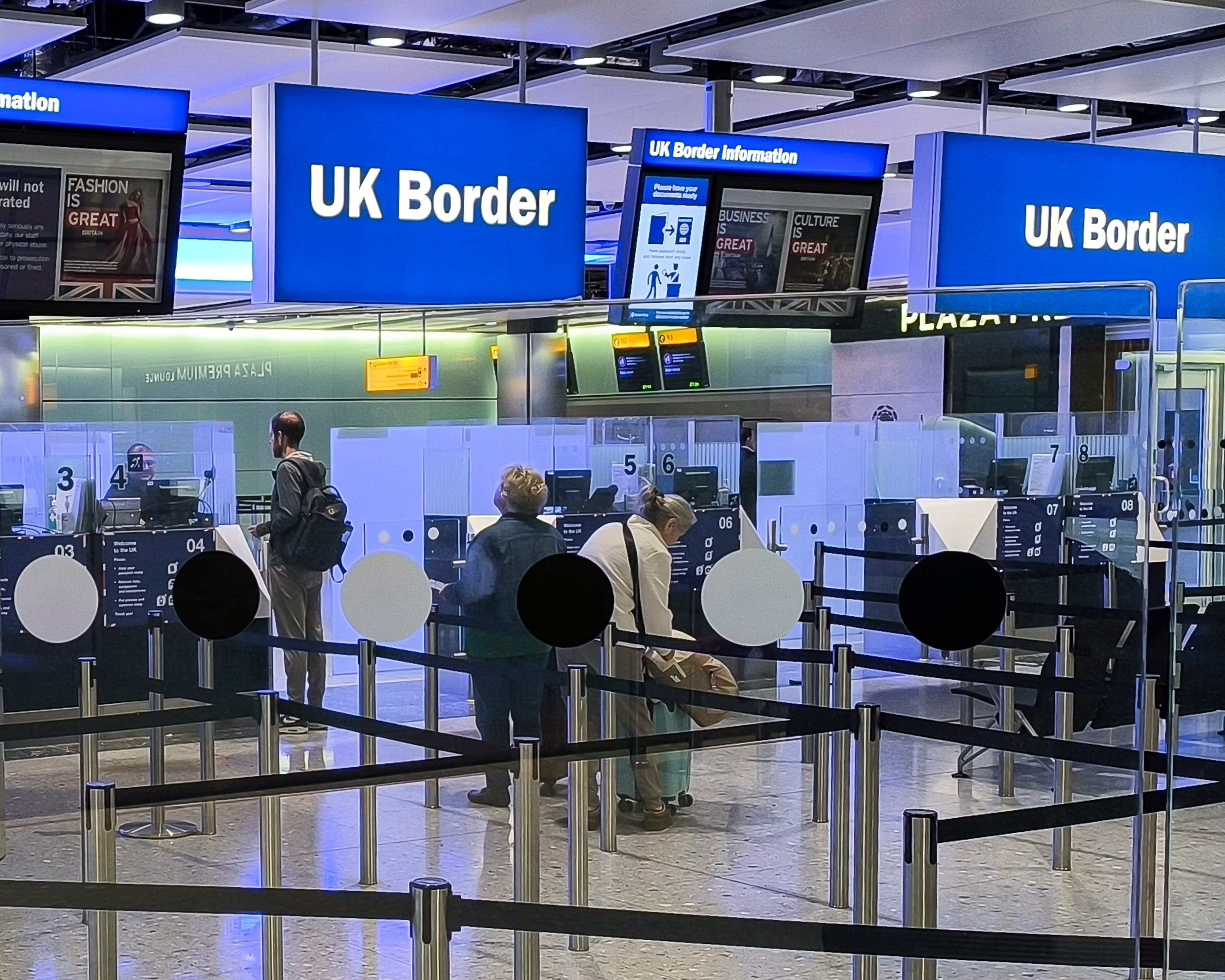 Viajeros hacen fila en los mostradores de control fronterizo bajo carteles de UK Border en un aeropuerto