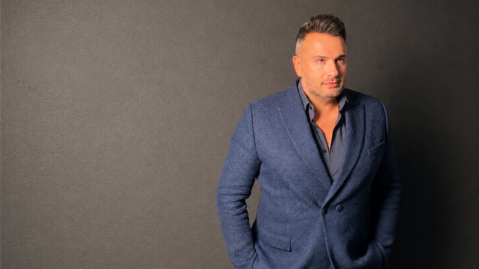 Maxim Berin fotografiado con una chaqueta azul texturizada ante una pared gris.