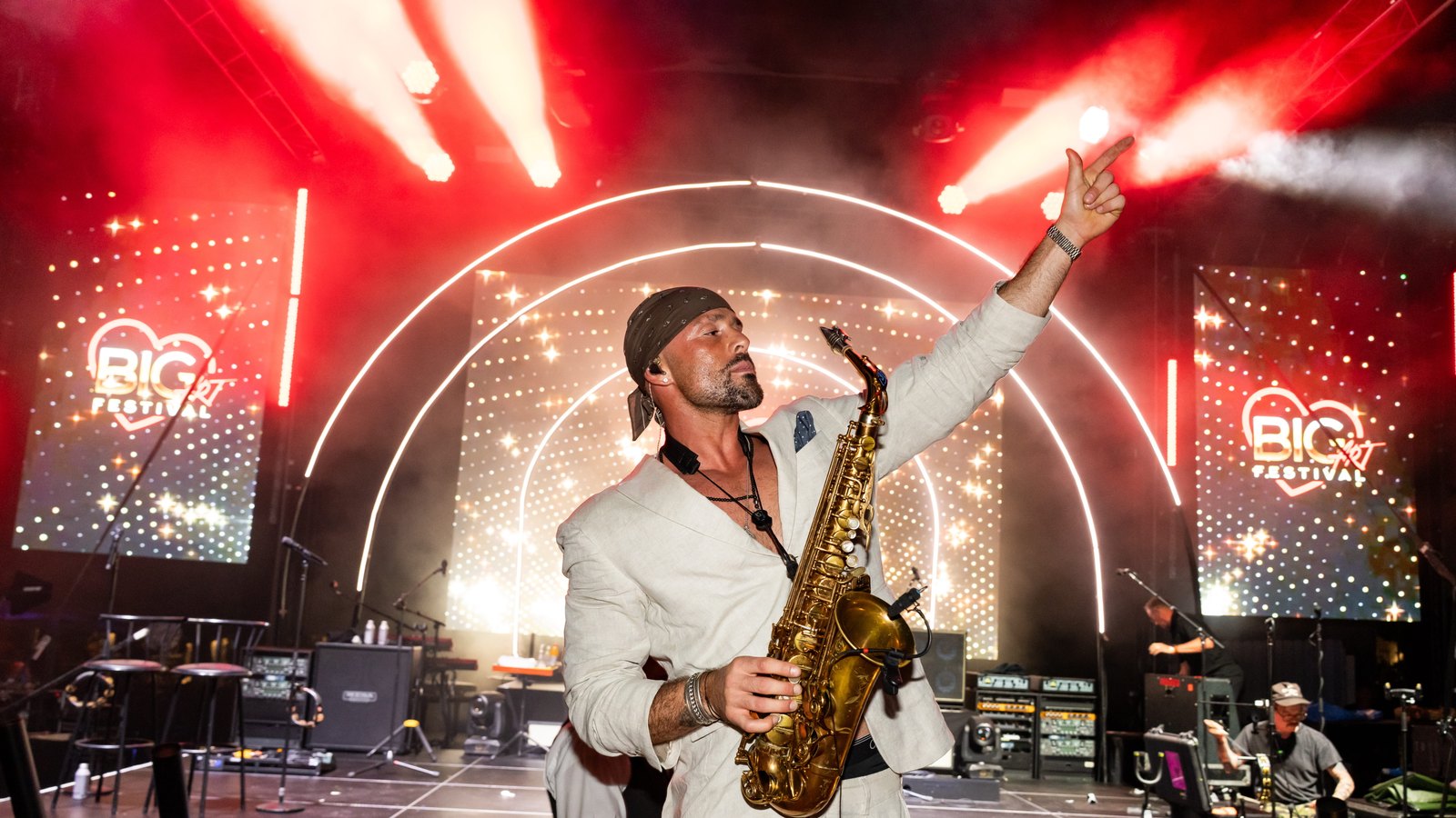 Max Merseny toca el saxofón en el escenario de BIG ART Festival, un brazo levantado, bajo una iluminación roja.